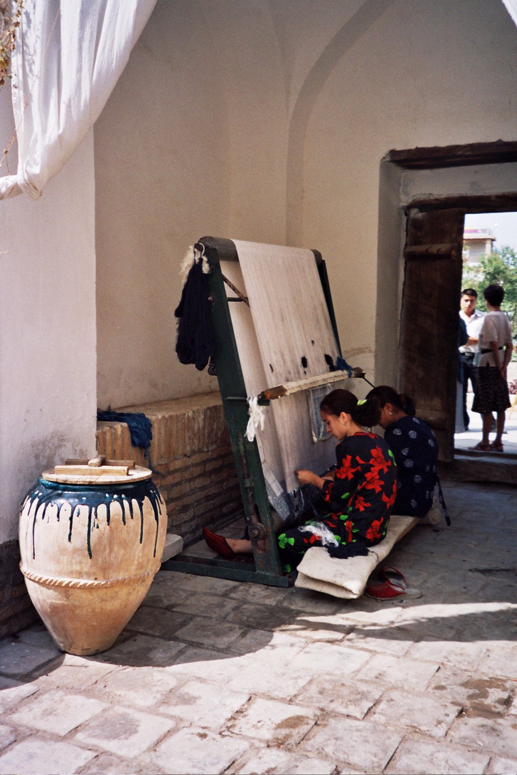 Weavers at a loom beside an indigo dye vat in a silk carpet workshop in Khiva