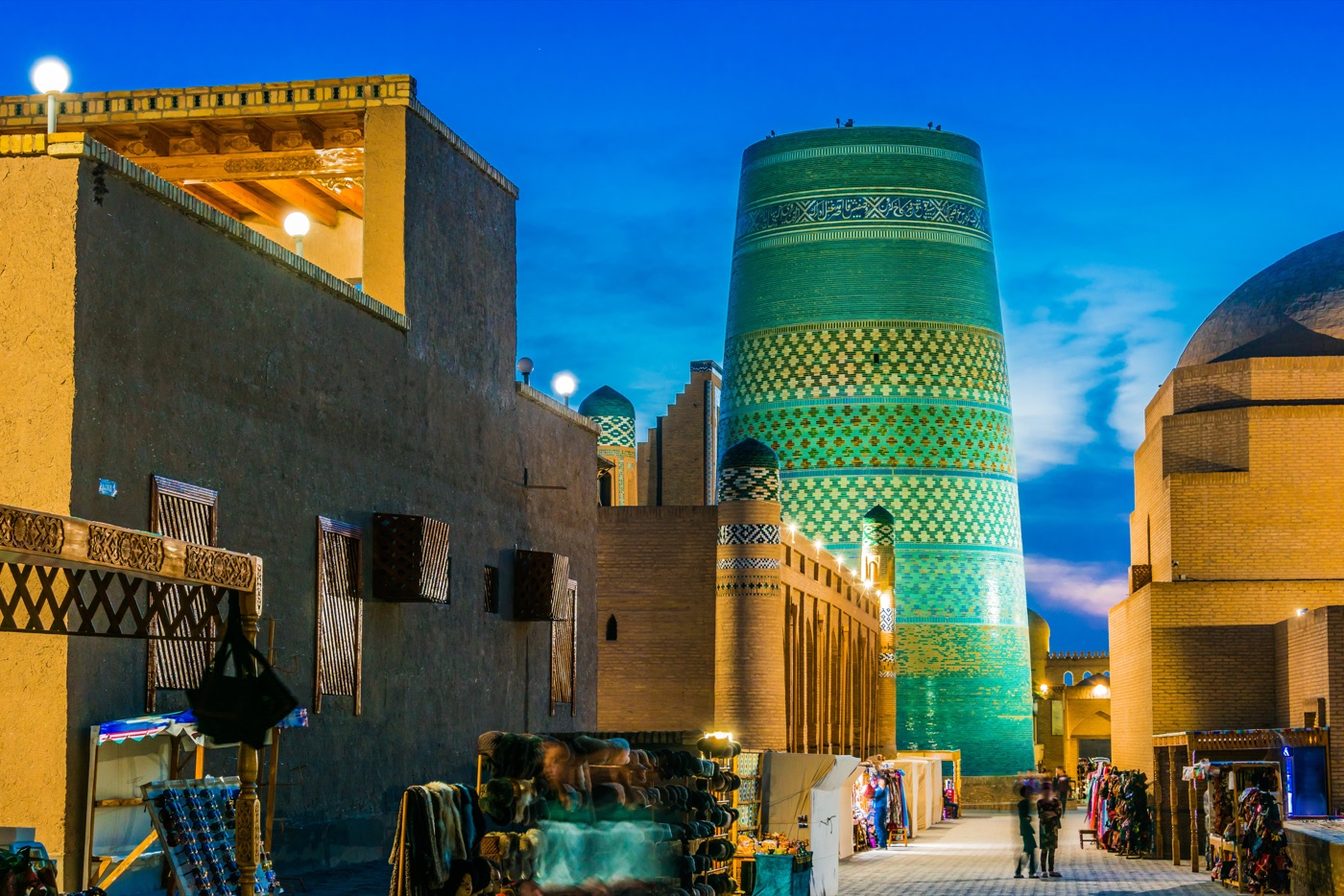 Lived-in rooftops of Khiva's old town at dusk near the Kalta Minor minaret, with household items and ladders visible